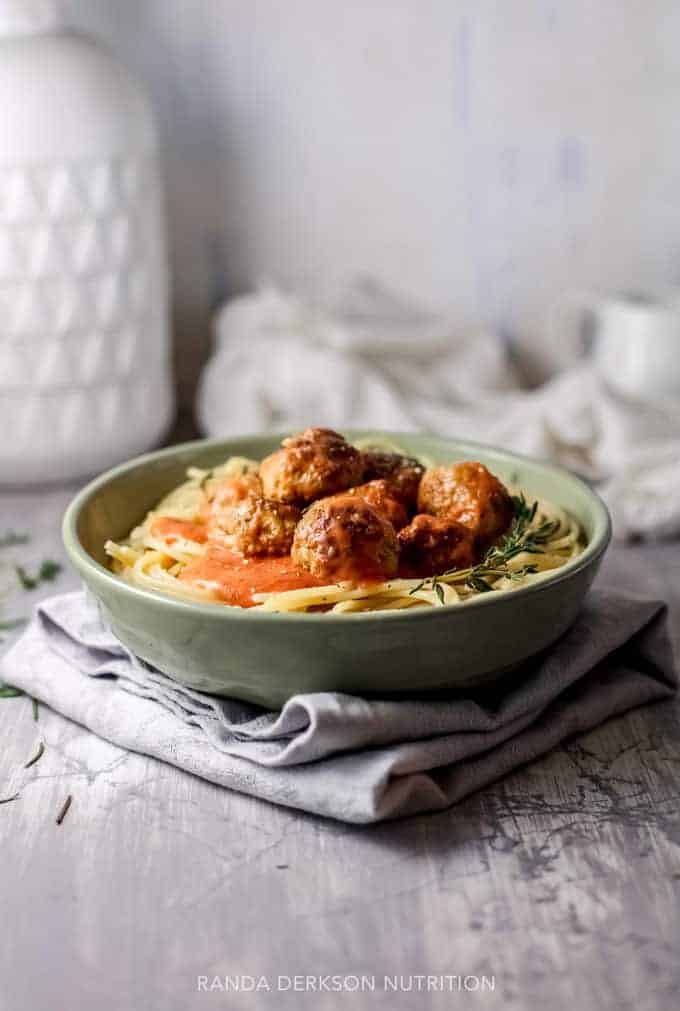 hidden vegetables in beef meatballs laying over pasta in a green bowl