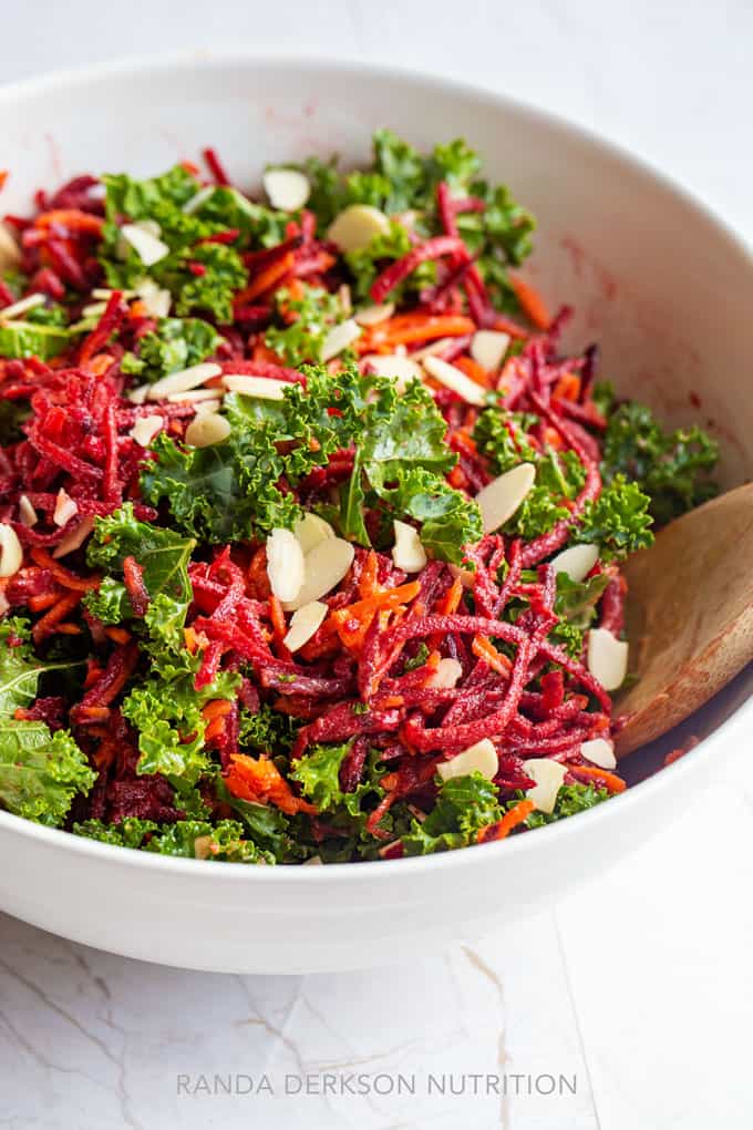 shredded beet, carrots, and kale in a white bowl tossed with vinaigrette and almonds