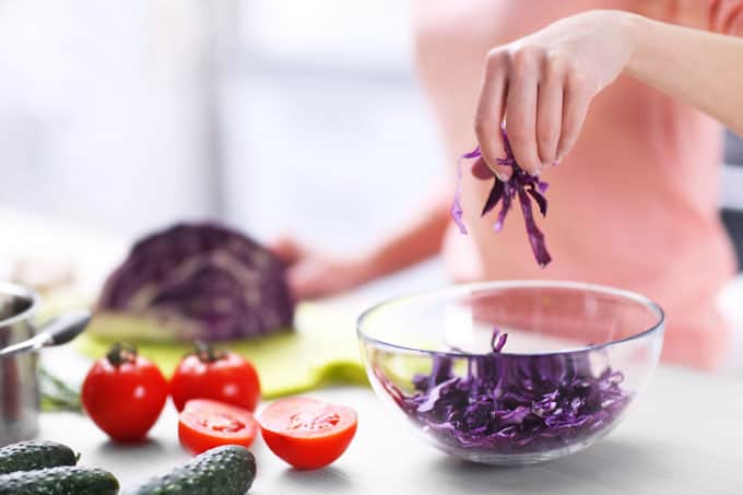 woman shredding purple cabbage and putting it in a bowl