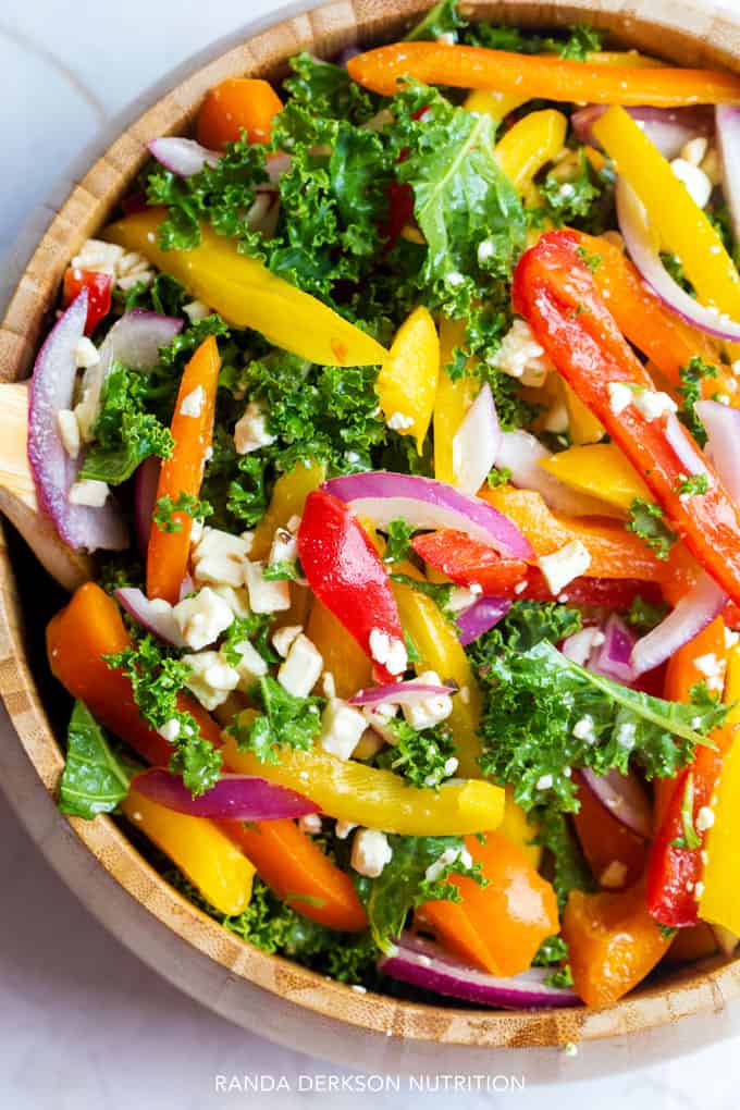 looking down on a wooden bowl with kale, bell peppers, feta cheese, and purple onion tossed together in a sesame rice vinaigrette