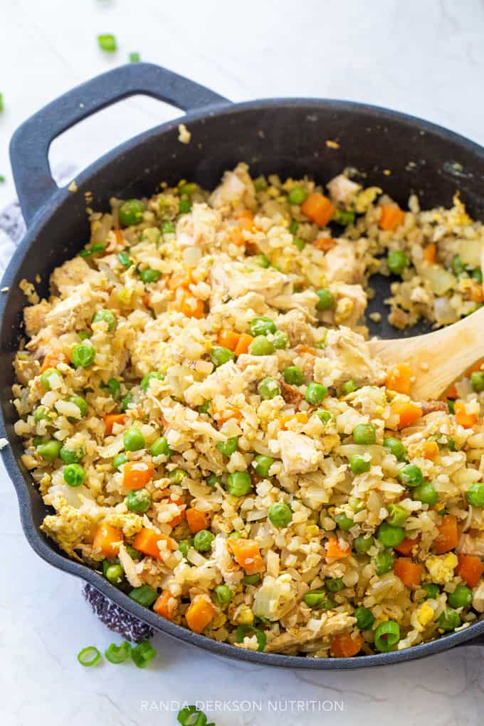 healthy chicken fried rice being stirred in a cast iron skillet