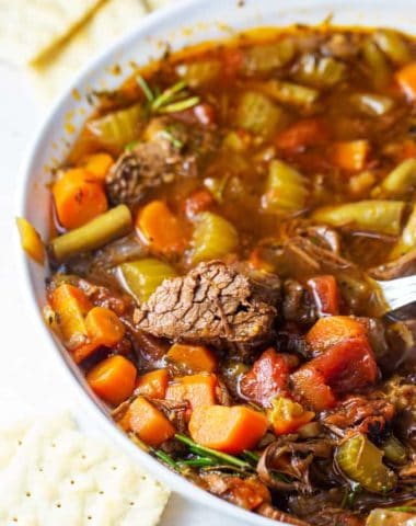 hearty beef and vegetable soup in a white bowl with crackers.