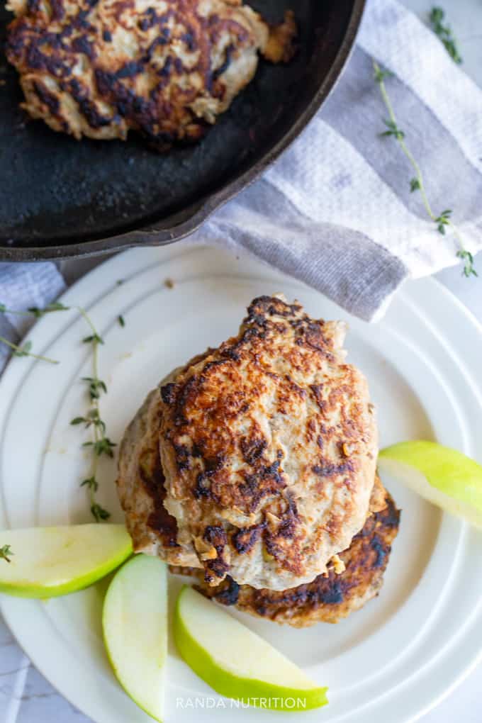 looking down on cooked chicken patties surrounded by sliced apples and a cast iron skillet