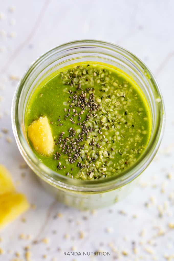 a top view of of a green smoothie in a mason har with pineapple, chia seed, and hemp seed garnish.