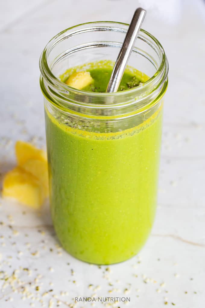 a side view of of a green smoothie in a mason har with pineapple, chia seed, and hemp seed garnish.