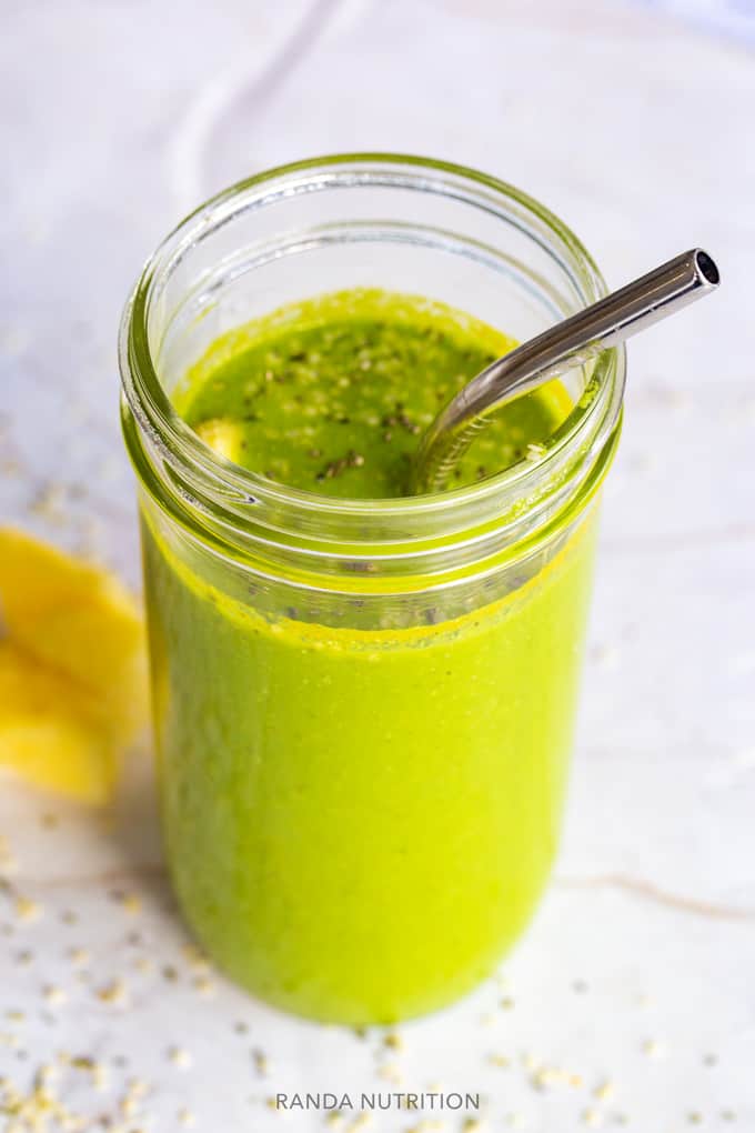 a side view of of a green smoothie in a mason har with pineapple, chia seed, and hemp seed garnish.