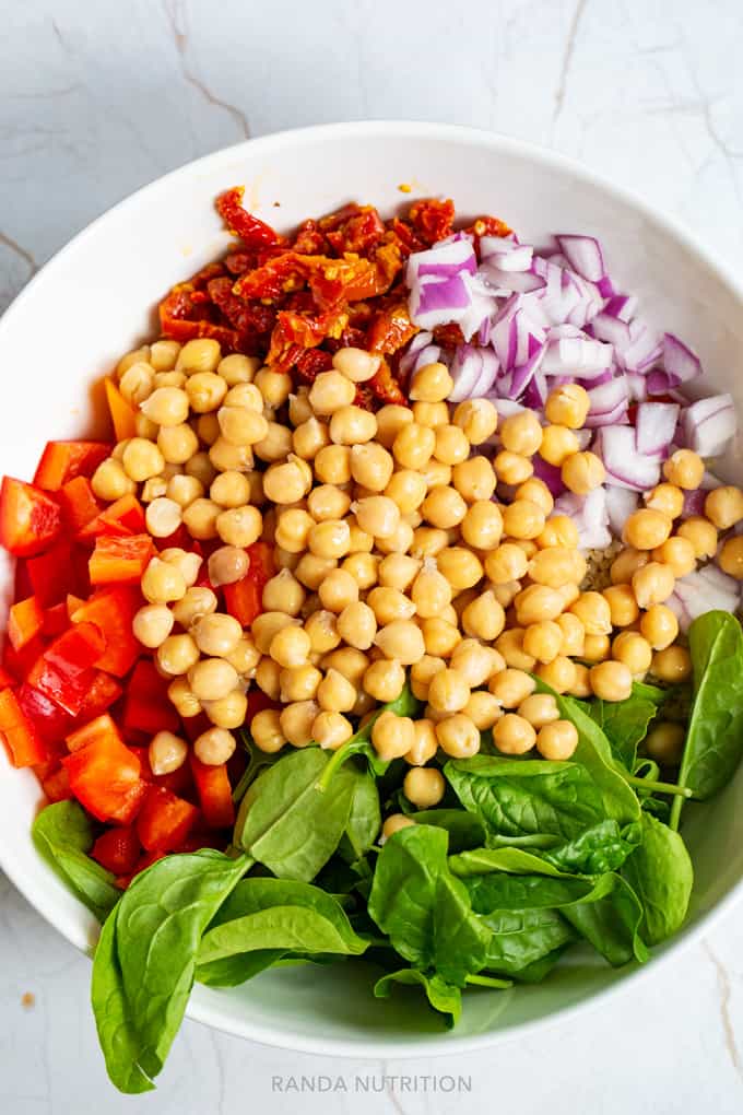 chickpeas, sundried tomatoes, bell peppers, spinach, and onion in a bowl ready to be tossed.