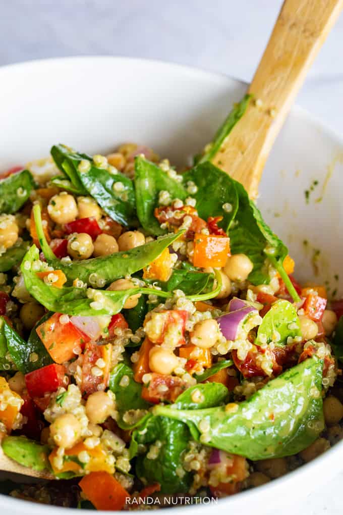 Tossing a healthy spinach quinoa salad with a wooden spoon