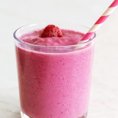 side view of a pink smoothie with a strawberry on top with a pink and white swirled paper straw