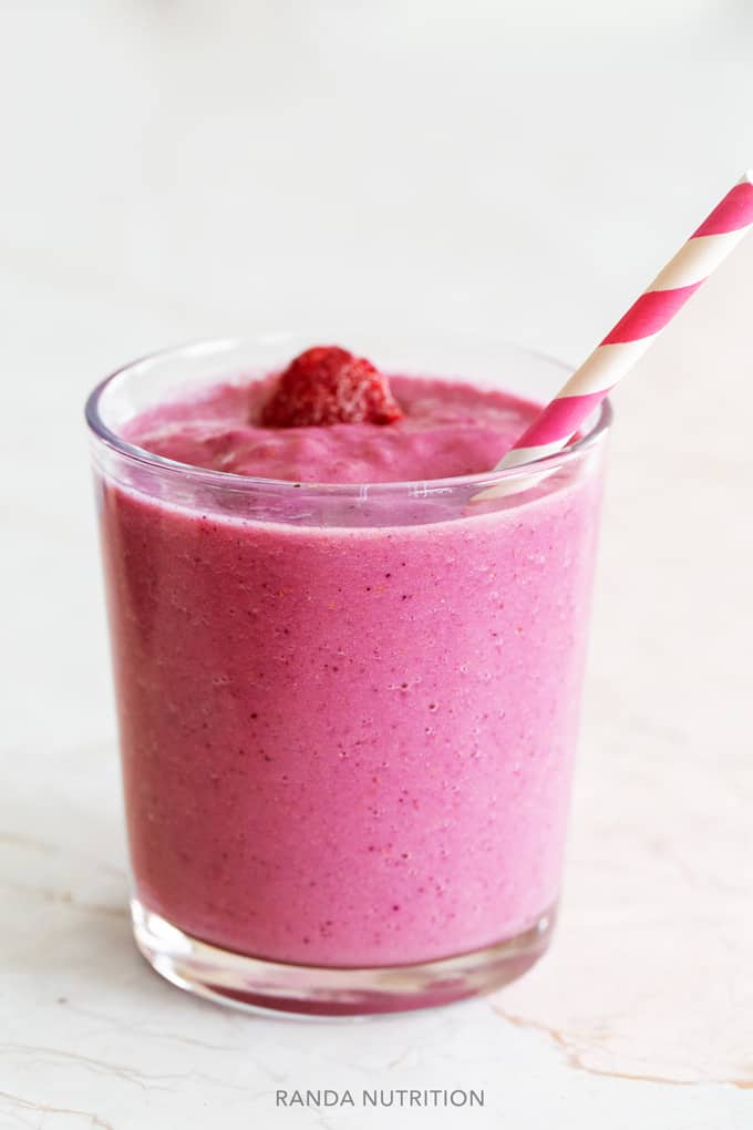 side view of a pink smoothie with a strawberry on top with a pink and white swirled paper straw