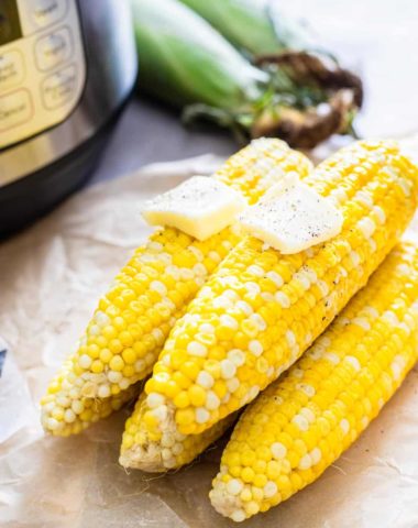 Five corn on the cob stacked on each other with two pats of butter.