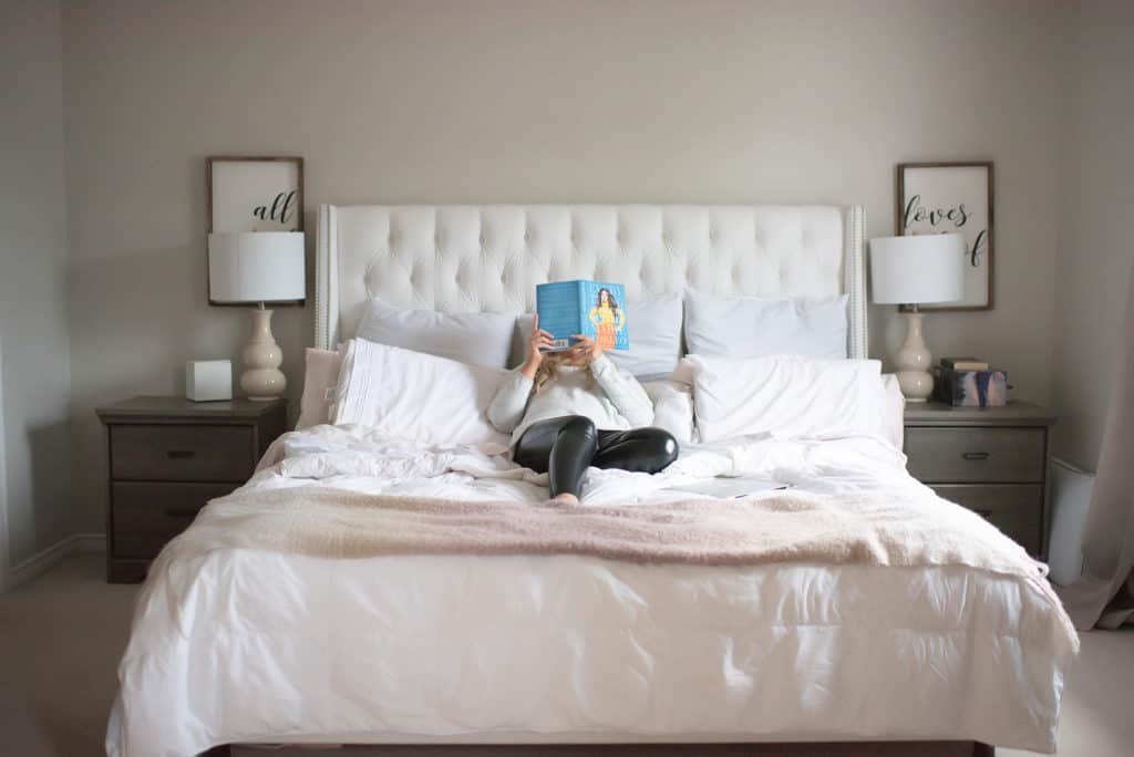 randa reading Marie Forleo's book while laying in a white tufted bed