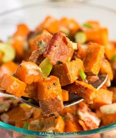 A spoon lifting sweet potato salad with pieces of bacon and a creamy dressing to the camera.
