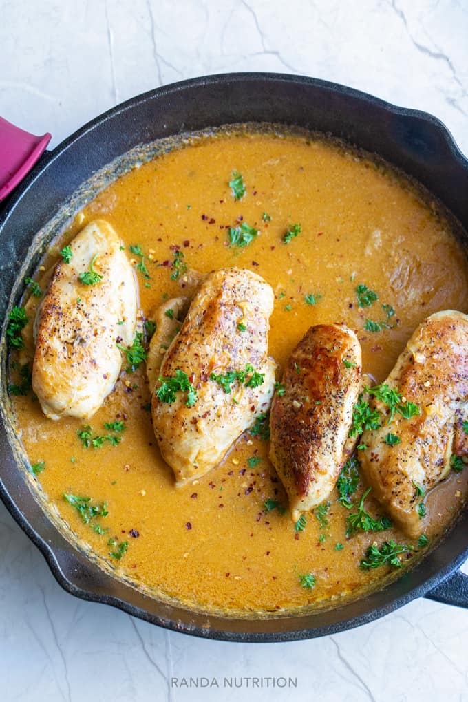 coconut curry chicken in a large cast iron pan simmering in coconut curry sauce