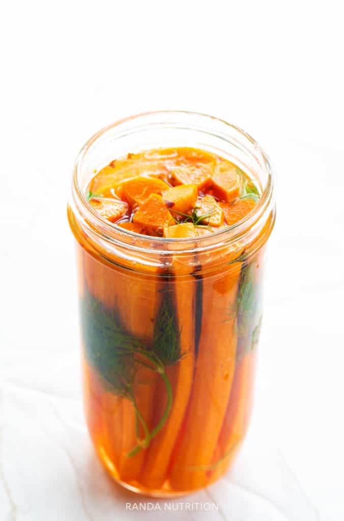 looking down at carrots, dill, and garlic in a vinegar brine in a mason har