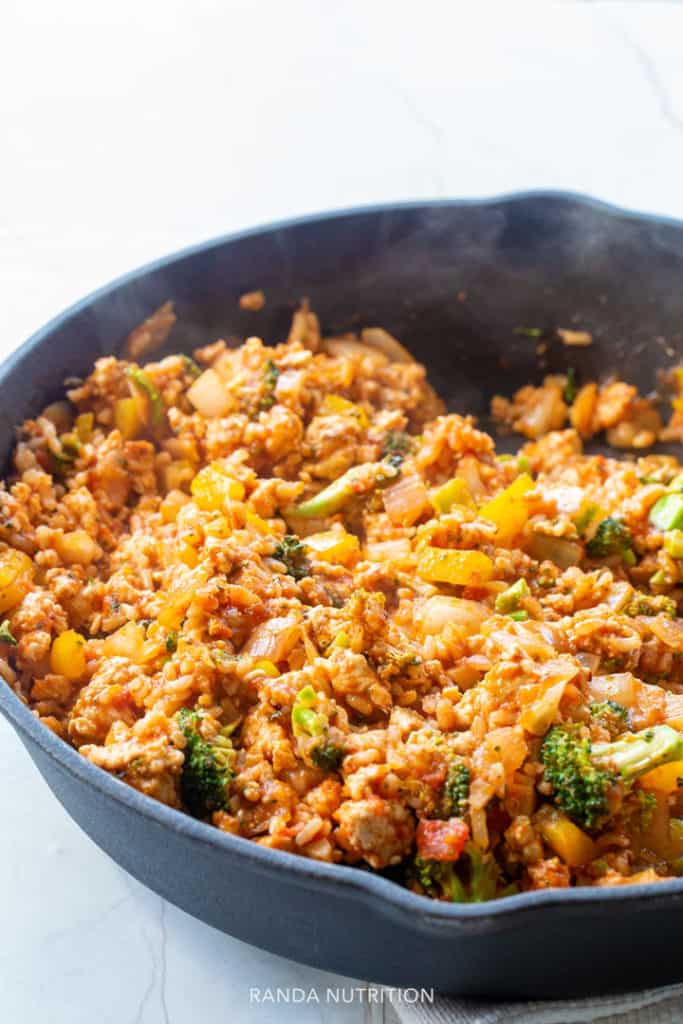 De vulling van gevulde paprika's die in een gietijzeren pan sist, bevat broccoli, zilvervliesrijst, kipfilet en marinara.