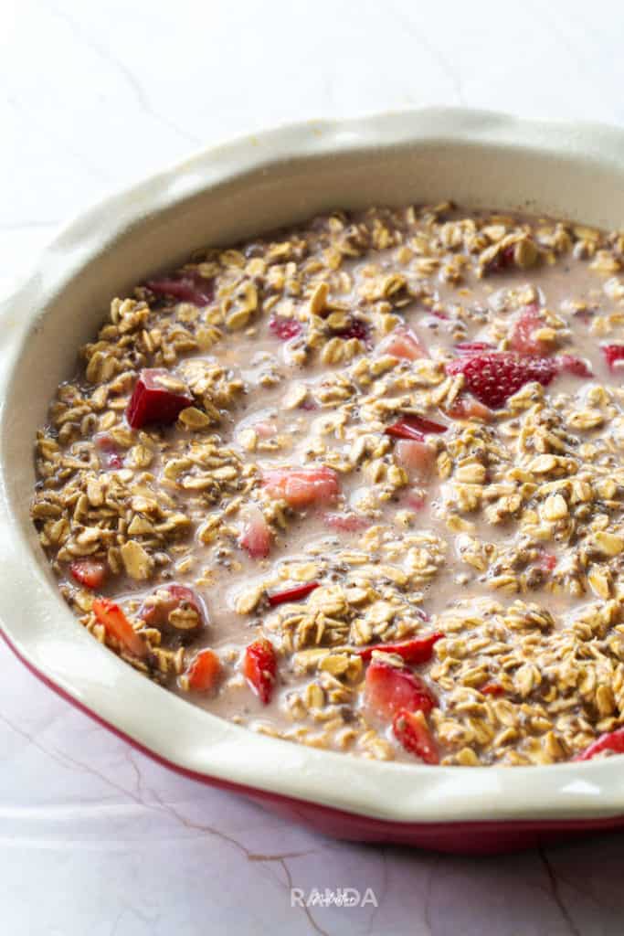 oats, rhubarb, strawberries, and almond milk mixed together and placed in a baking dish about to be placed in the oven