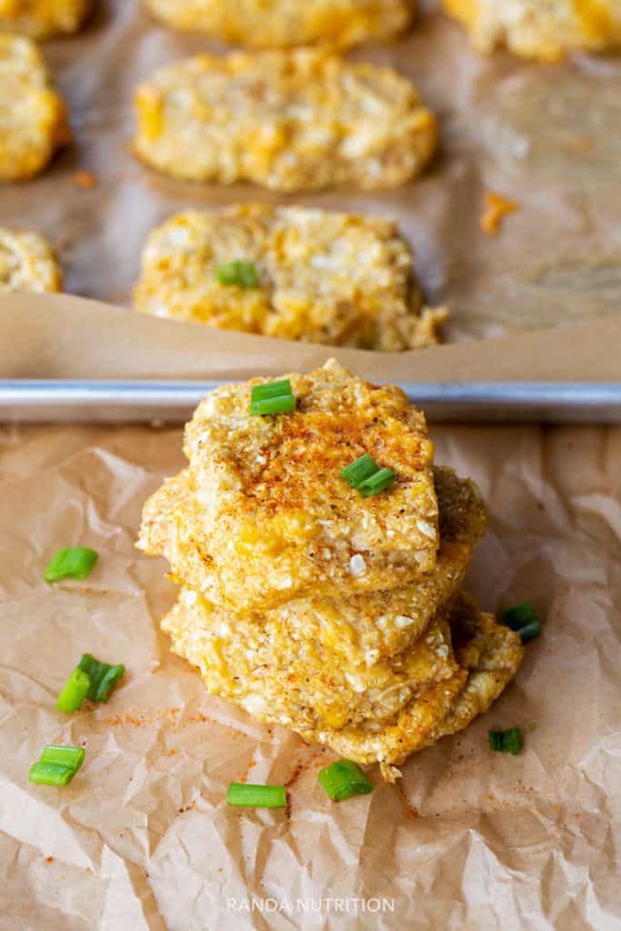 a stack of cauliflower hashbrown patties on a lined baking sheet