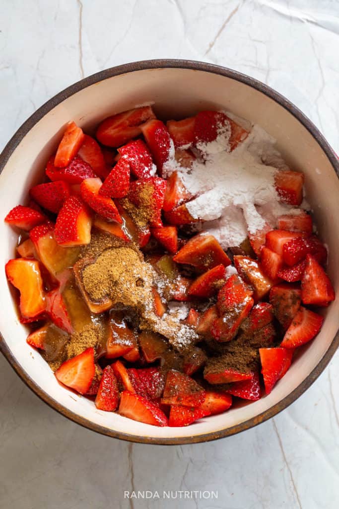 strawberries, rhubarb, coconut sugar, honey, arrowroot powder in a dutch oven ready to be reduced to a sauce