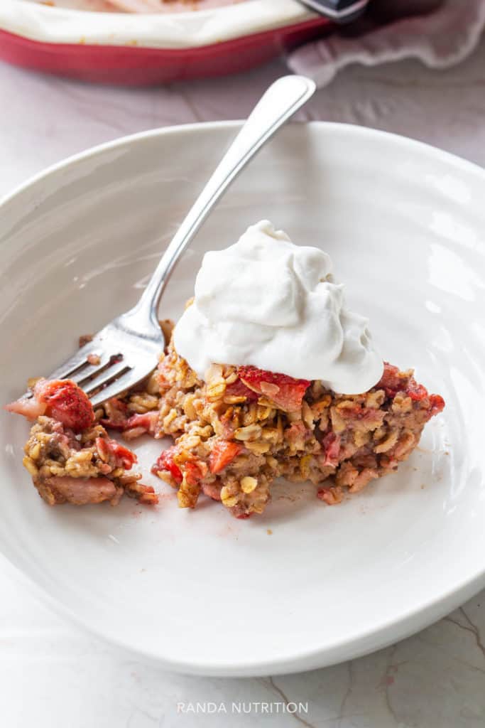 A piece of oatmeal casserole sliced into with a fork, topped with whipped cream