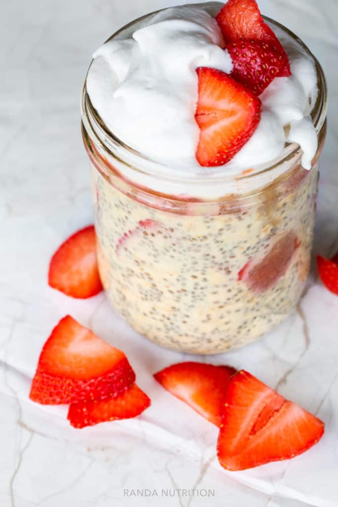 overnight oats topped with coconut whipped cream and strawberries in a mason jar