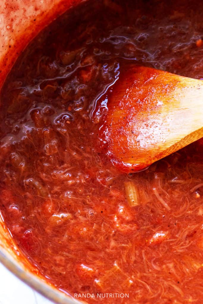 strawberry rhubarb pie filling in a dutch oven being stirred by a wooden spoon