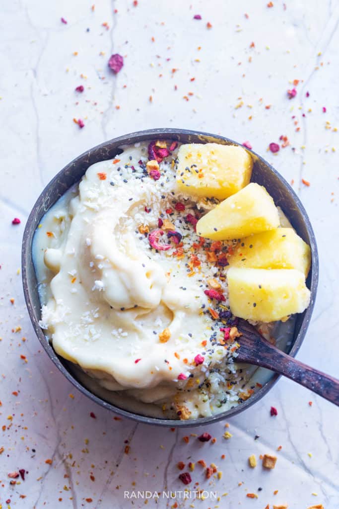 Homemade dairy free ice cream in a coconut bowl topped with pineapples and coconut