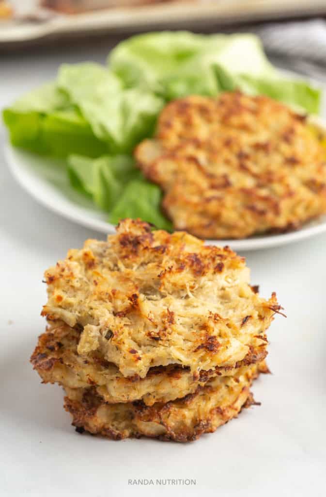 baked crab cakes stacked on top of each other with one on a bed of lettuce in the background