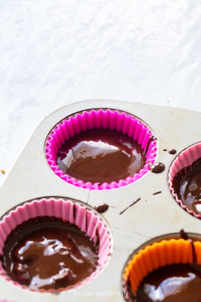 peanut butter cups being set in a muffin tin with multicolored liners