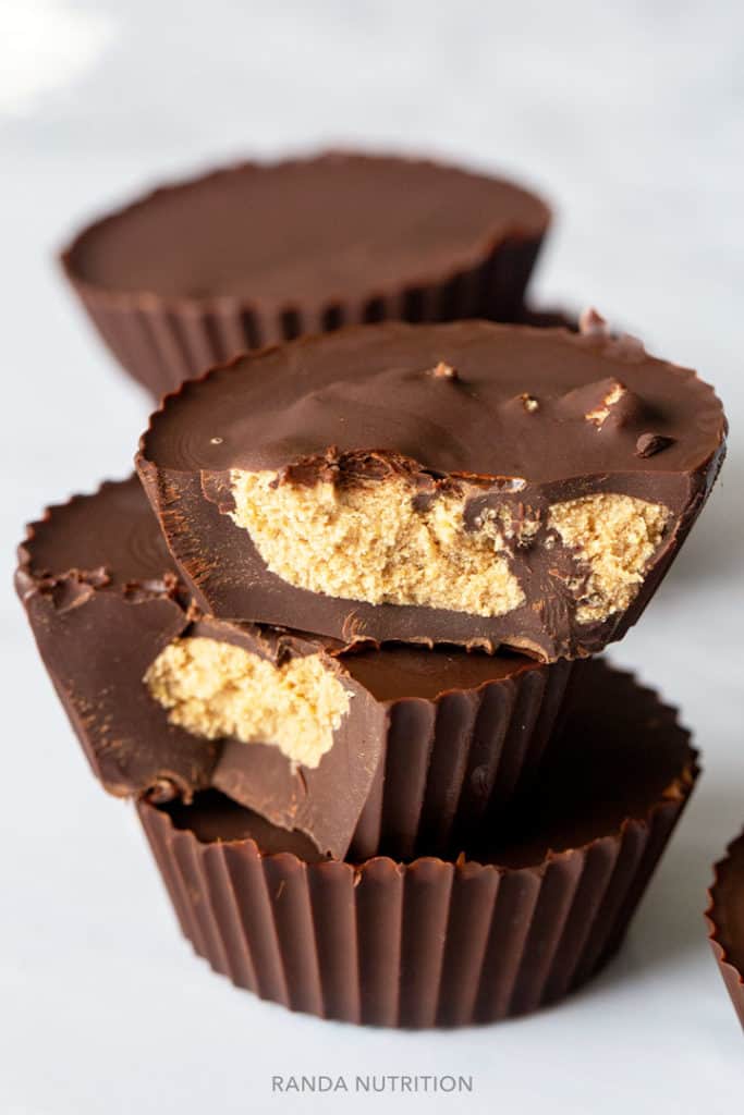 chocolate peanut butter cups stacked on each other with a bite taken out of two showing the protein peanut butter center