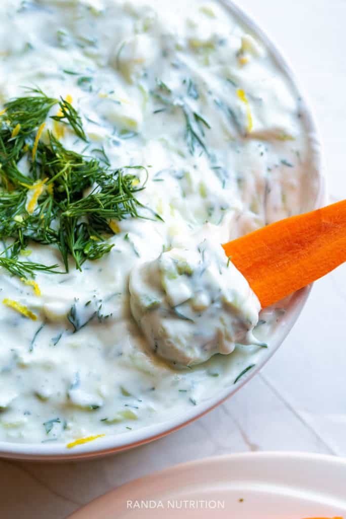 a carrot scooping out tzatziki sauce out of a bowl