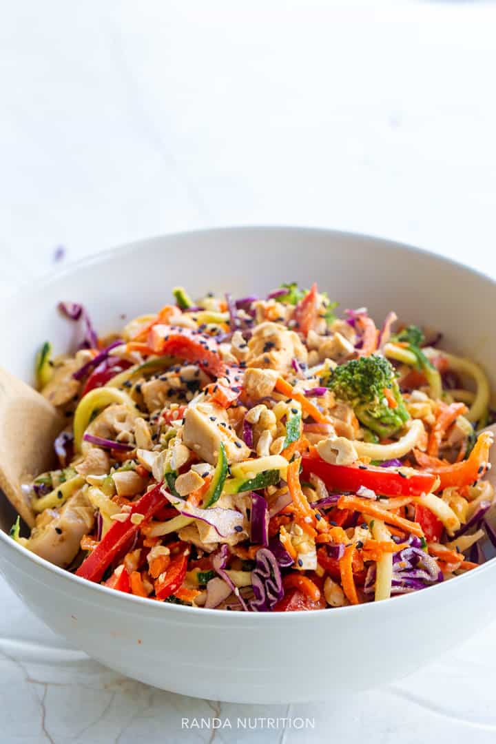 Close up of Thai Chicken Veggie Noodle Salad with Creamy Peanut Dressing in white serving bowl with colorful veggies on top
