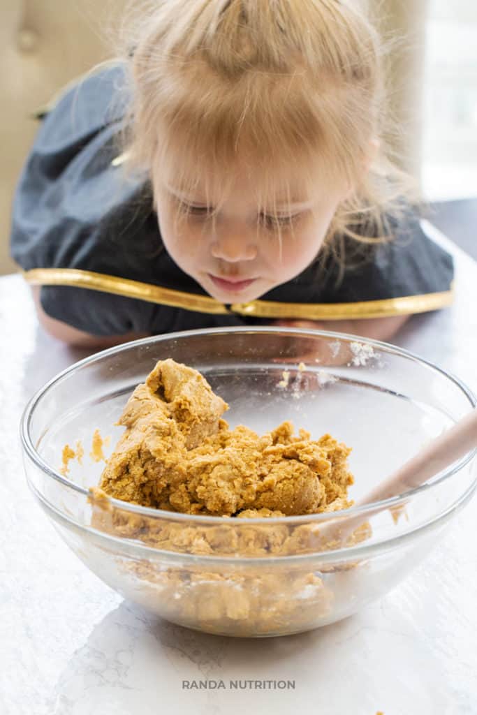 toddler looking into a glass bowl with pumpkin muffin batter