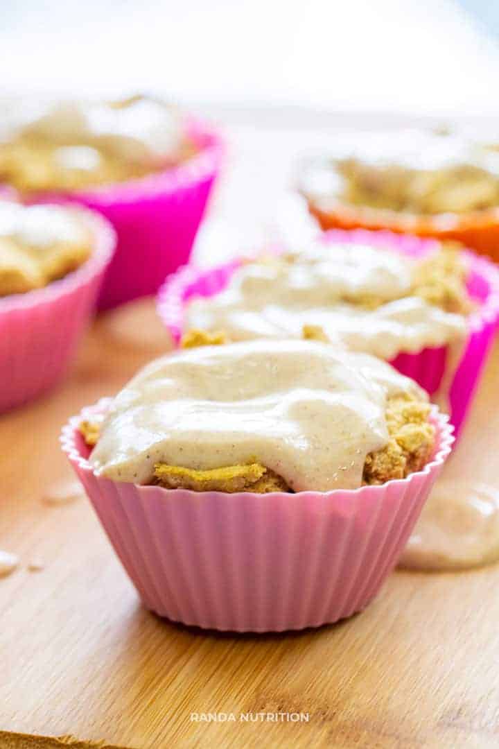 pumpkin yogurt frosting over a muffin in a pink silicone liner.