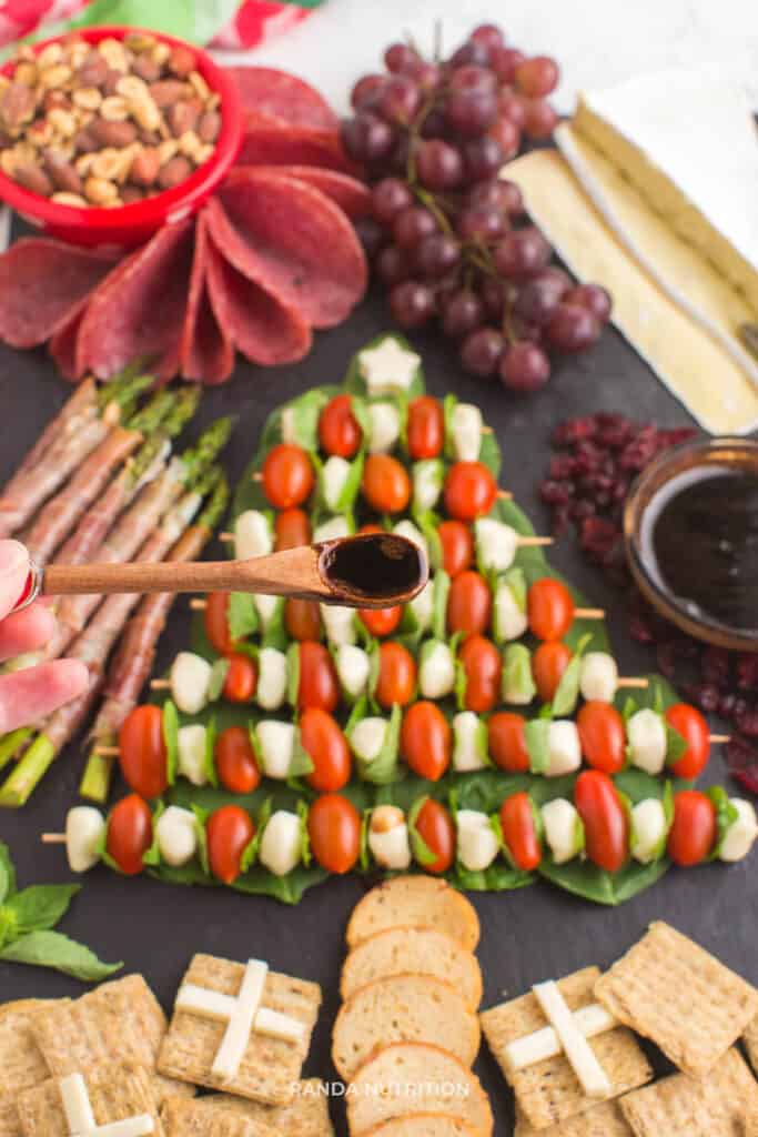 a wooden spoon lifting balsamic glaze ready to frizzle over fresh tomatoes, basil, and mozzarella balls