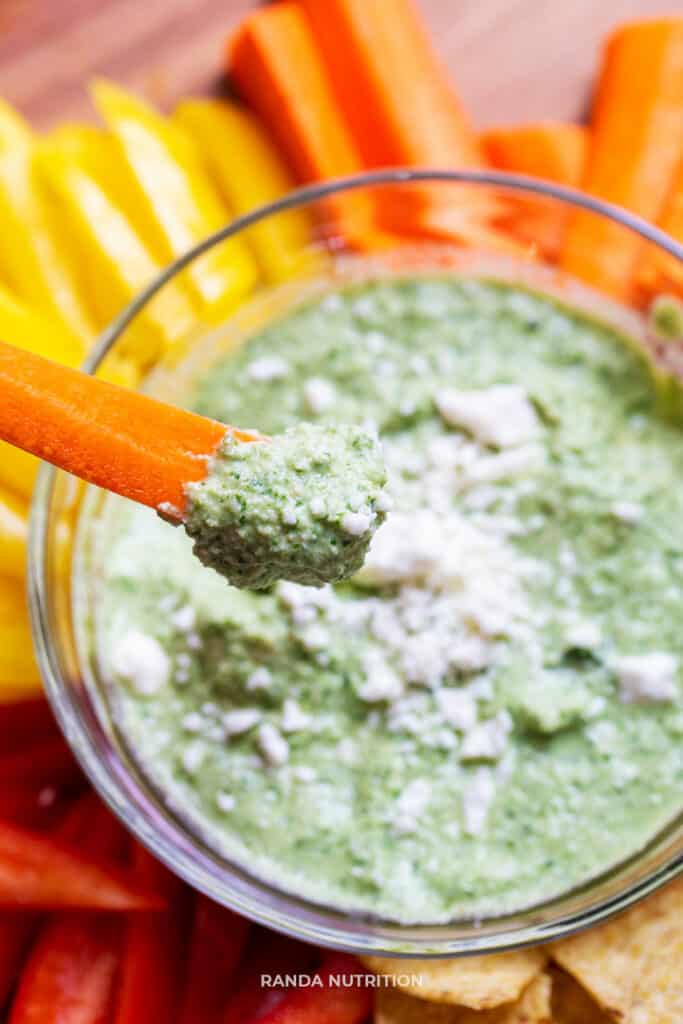 a carrot stick with a green dipping sauce being lifted off the wooden platter