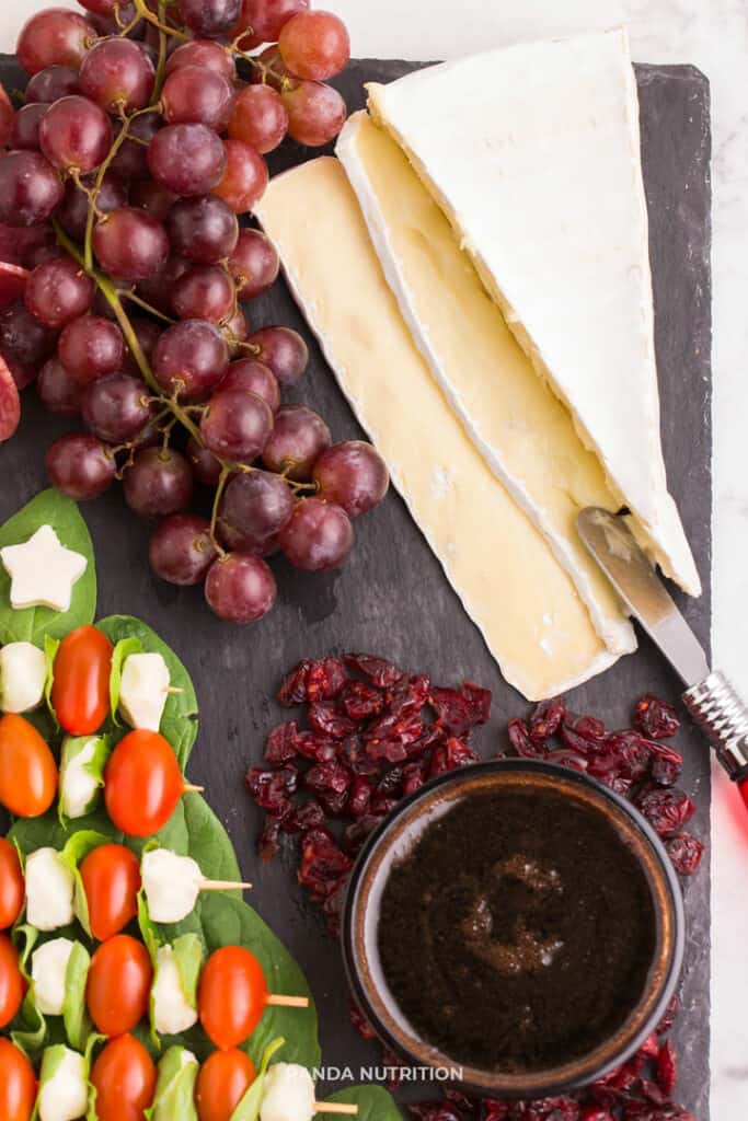 brie, grapes, and balsamic glaze on a slate for appetizersThis simple DIY Christmas Tree Caprese Board is such an easy idea! If you're wondering how to make a charcuterie board that will appeal to a crowd (keto, healthy, and vegetarian) this holiday meat and cheese platter has something for every lifestyle. Added mozzarella, tomatoes, and basil for a cheese board that will be the best Christmas party appetizer ideas! #charcuterieboard #capreseboard #christmasparty