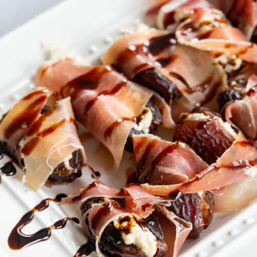 stuffed dates with a balsamic reduction drizzled over top of a white platter
