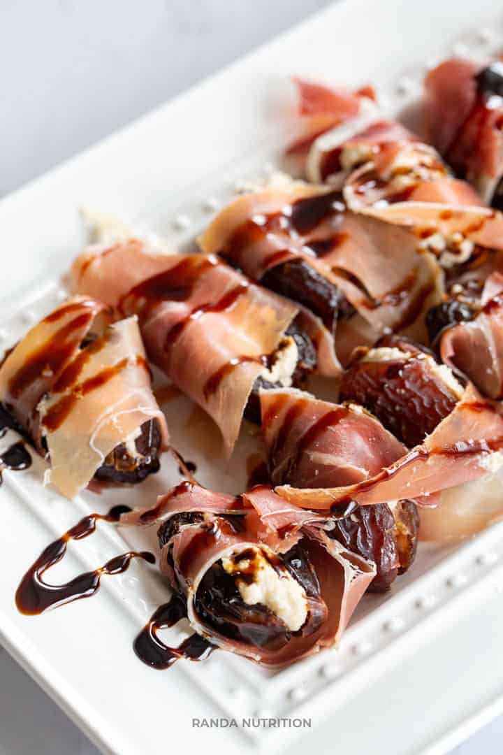 stuffed dates with a balsamic reduction drizzled over top of a white platter