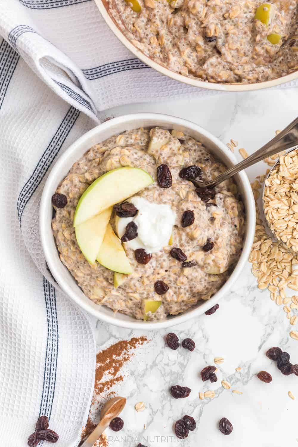close up of a fable bowl with cooked chia oatmeal with raisins, greek yogurt, and apples