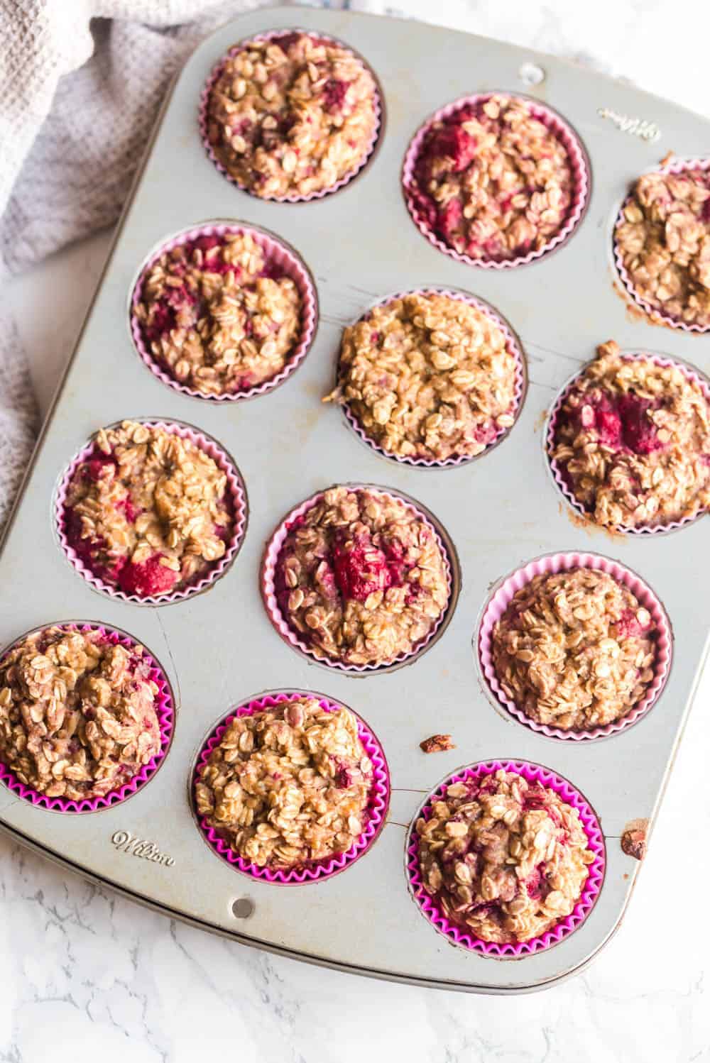 fresh baked raspberry protein oatmeal muffins in a tin with pink silicone liners