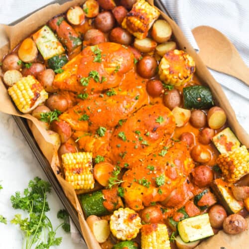 roasted chicken and vegetables on a sheet pan lined with parchment paper with a red pepper sauce drizzled over top