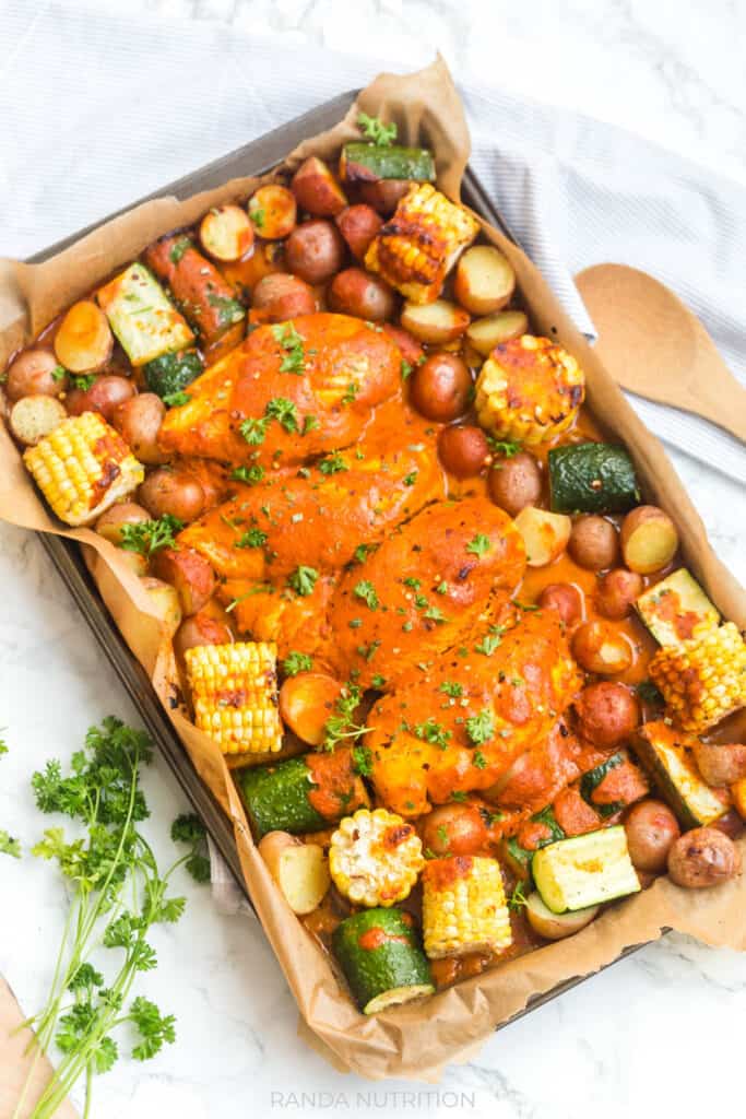 roasted chicken and vegetables on a sheet pan lined with parchment paper with a red pepper sauce drizzled over top