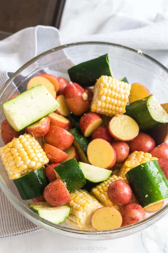 corn, zucchini, and baby red potatoes in a bowl with olive oil and salt and pepper