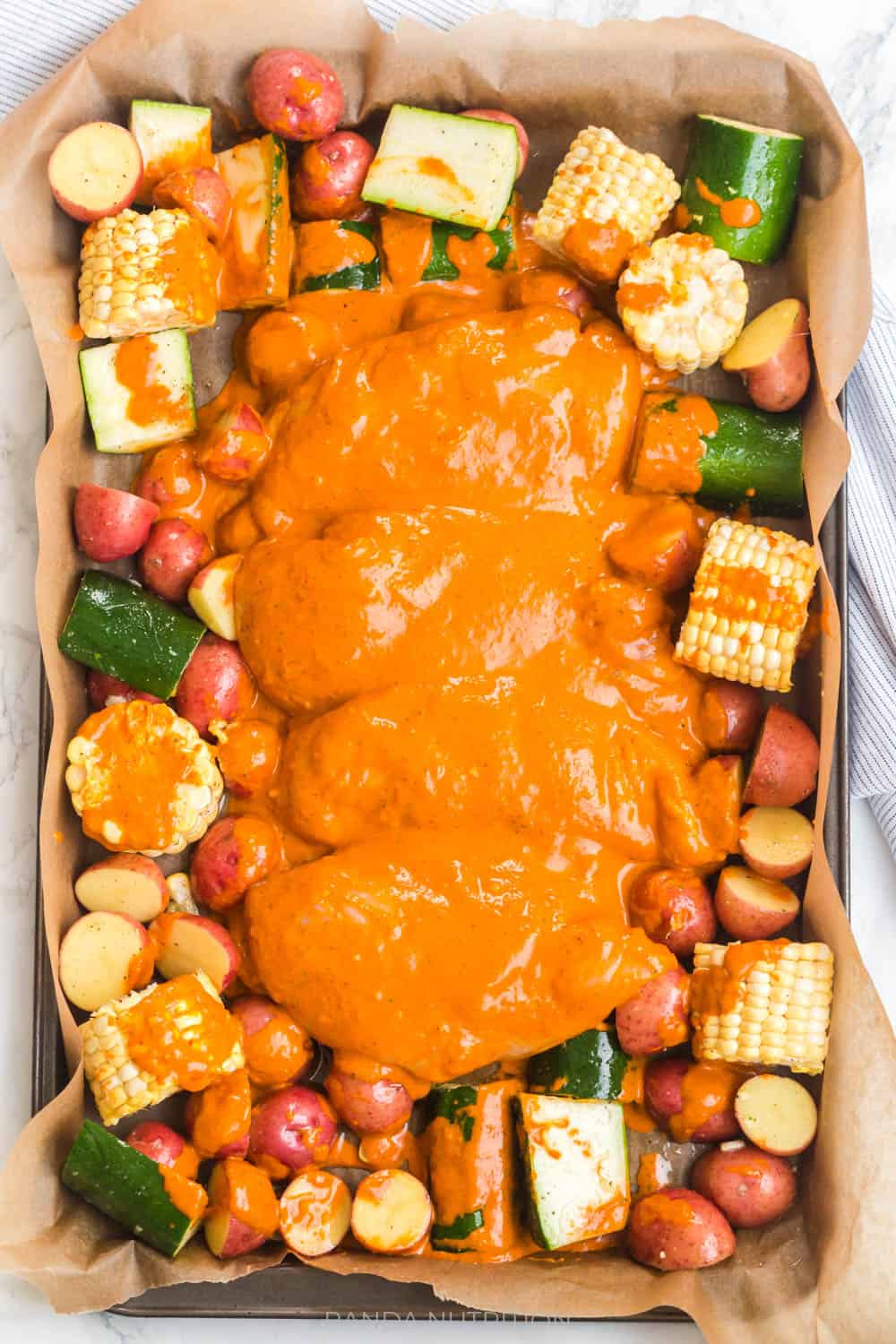 red pepper sauce poured over raw chicken and vegetables about to go in the oven