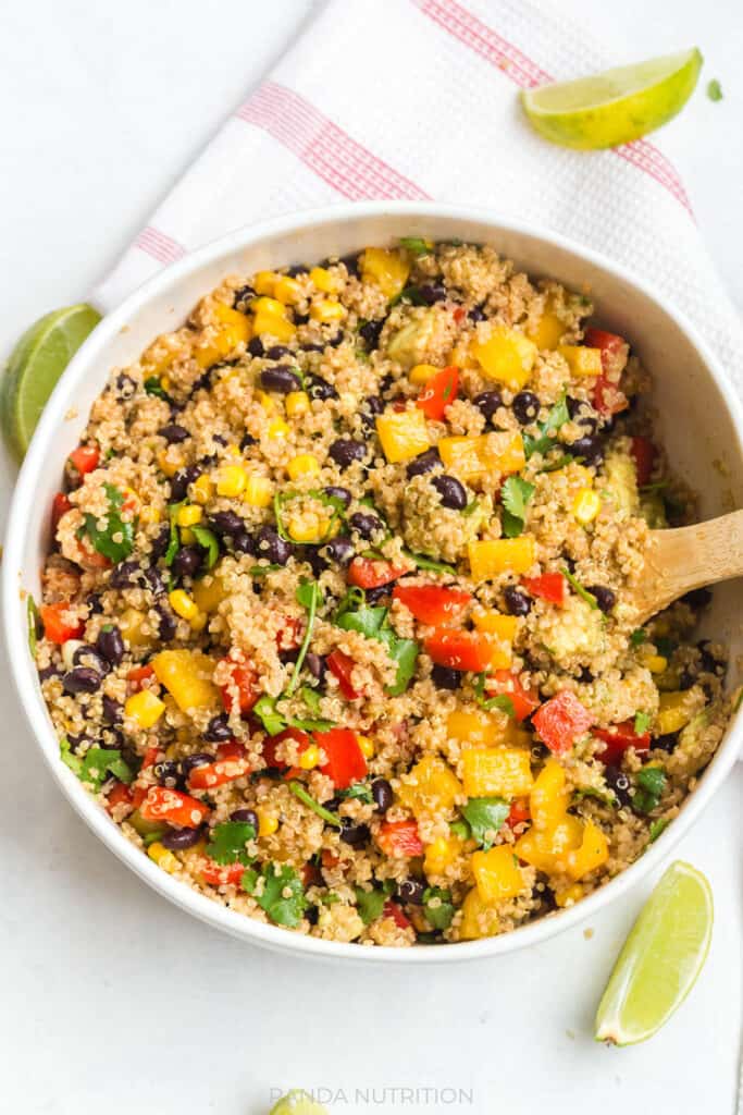 a large bowl with quinoa salad with black beans and limes being tossed with wooden spoons