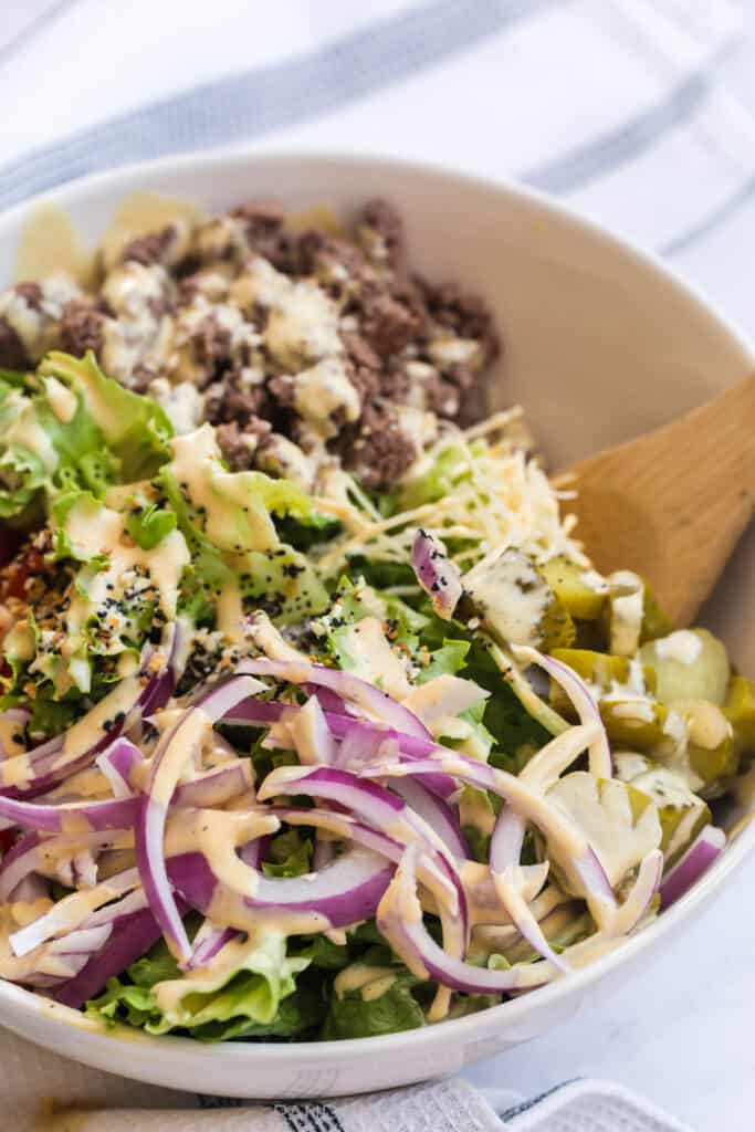 side shot of red onion with dressing on it in a burger bowl