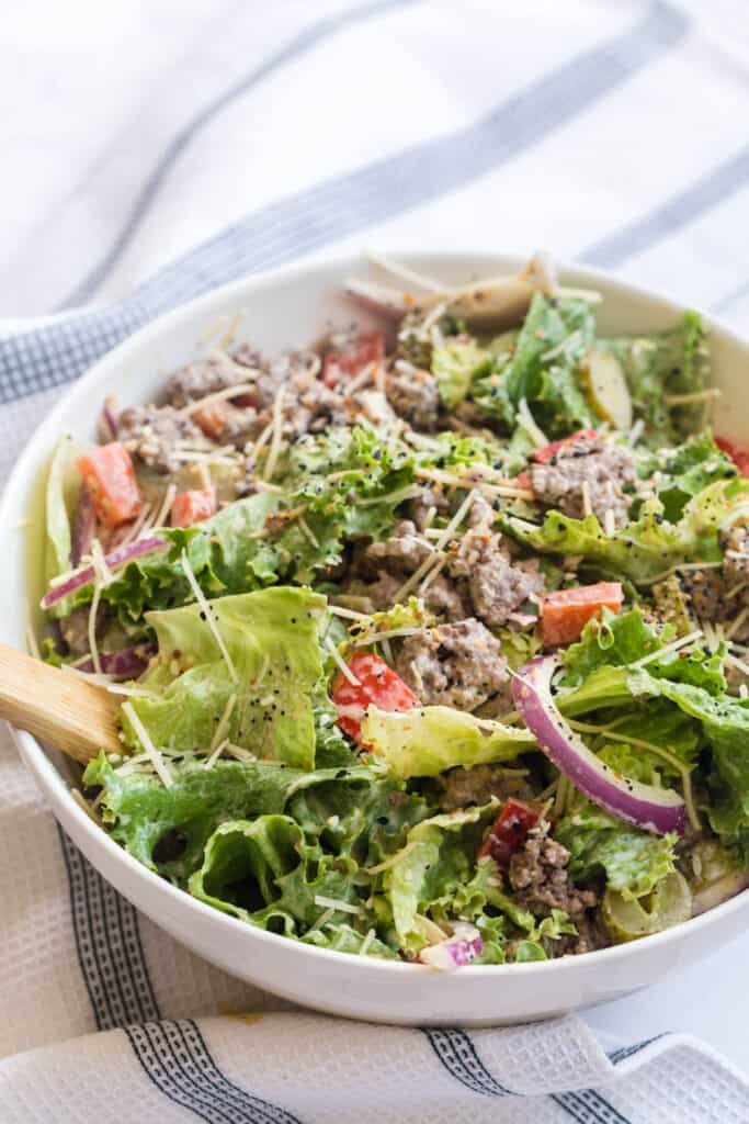 salad with ground beef being tossed in a bowl.