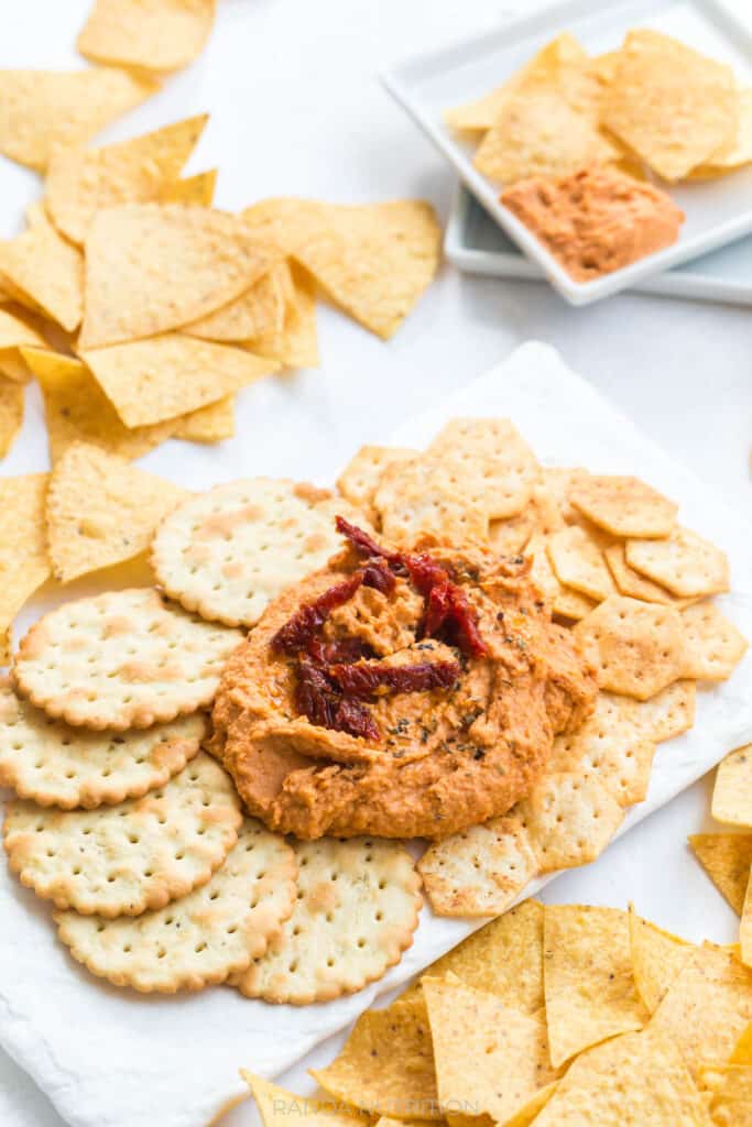 angle view of sun dried tomato hummus on a white slate platter surrounded my crackers for a party