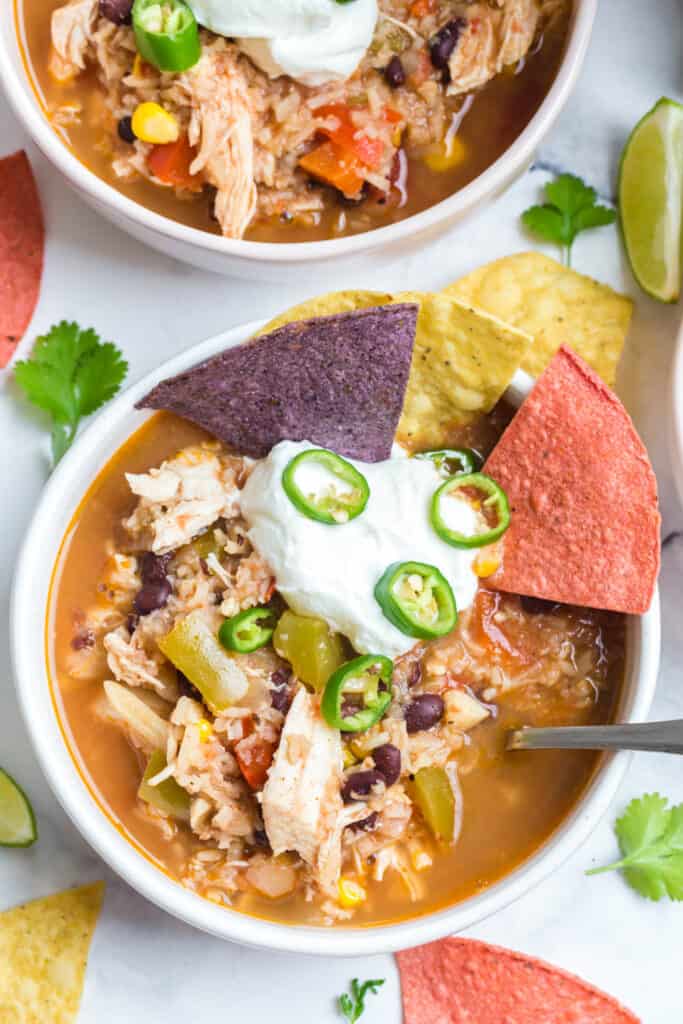 a bowl of this instant pot southwest chicken soup served with plain Greek yogurt, tortilla chips, and sliced jalapeños with more bowls of soup in the background